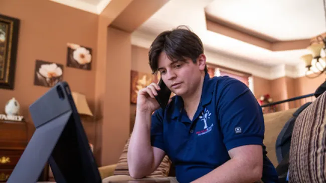 Young man using a smartphone and tablet while sitting on a couch in a cozy living room.
