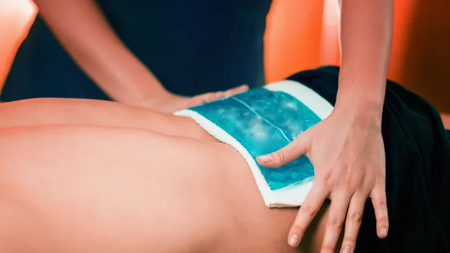 Therapist applying a blue cold compress on a person's lower back for pain relief and recovery.