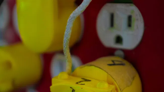 Close-up of yellow electrical connectors with red and blue wires attached on a red panel with numbered labels.