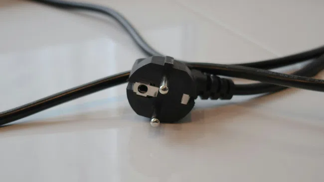 Close-up of a black European two-pin electrical plug on a white surface with attached cable.