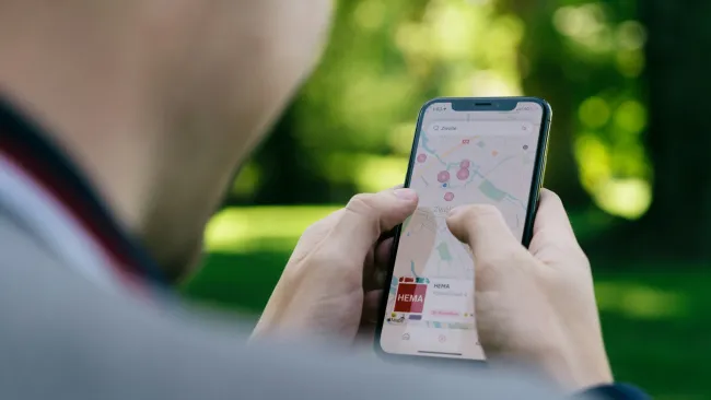 Person using smartphone to navigate a map application outdoors with green blurred background.