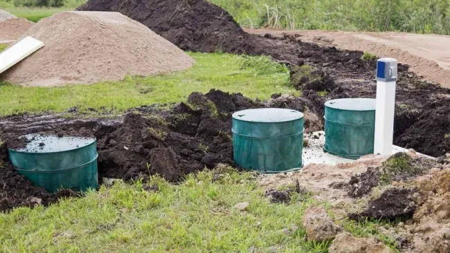 Green septic tank system installation with piles of soil and sand nearby on a grassy field.