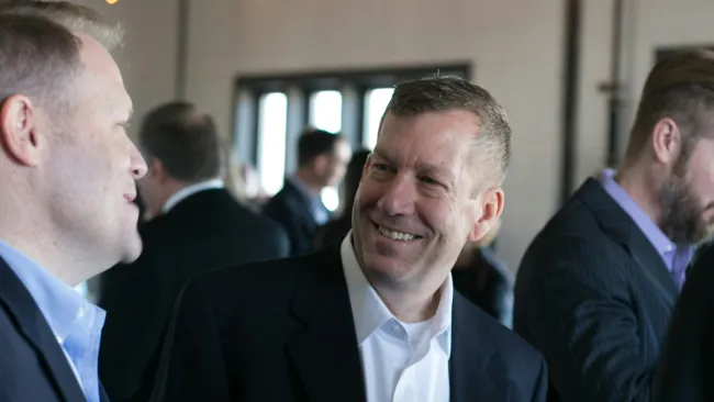 Two men in business attire chatting at a social event with twinkling lights above.
