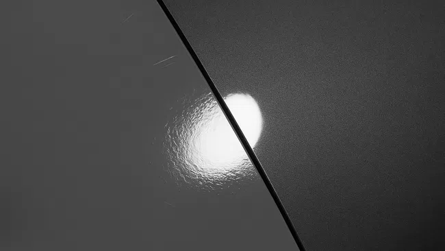 Close-up of light reflection on contrasting matte and glossy dark surfaces divided by a sharp line.