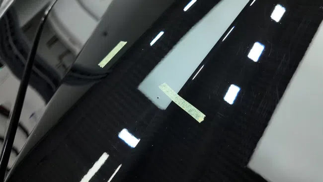 Close-up of a black glossy surface with light reflections and a small white tape marker.