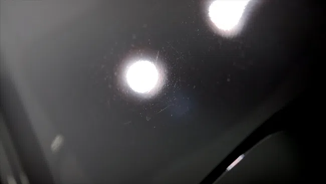 Close-up of dark glossy surface showing light reflections and fine scratches or dust particles.