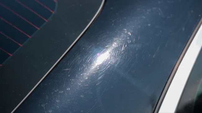 Close-up of car paint surface with visible swirl marks and scratches under sunlight reflection on dark blue finish