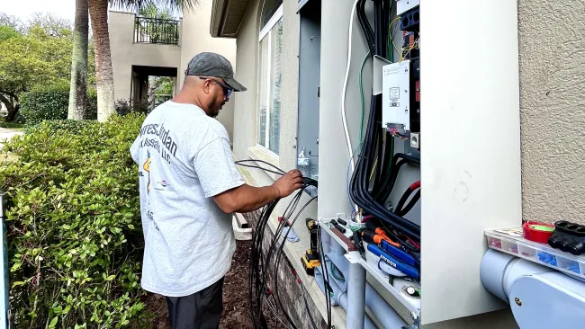 Electrician working on outdoor electrical panel wiring next to residential home while installing a home standby Generac generator. 22kW 26Kw