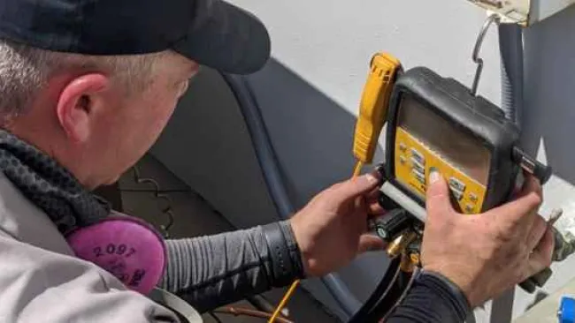 Technician adjusting HVAC system using a digital gauge manifold outdoors in daylight.