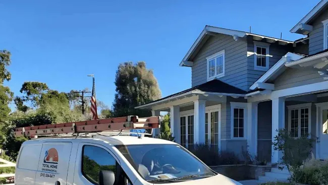 White work van with ladder on roof parked in driveway of modern suburban home under clear blue sky.