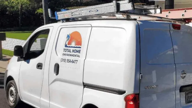 White service van with ladder on roof and Total Home Environmental logo parked on street by palm trees.