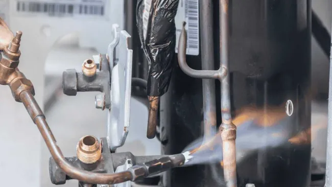Close-up of HVAC equipment with a flame heating copper pipes attached to a compressor unit.