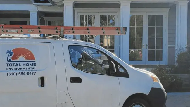 White Total Home Environmental van with a ladder on top parked in front of a large gray house with white trim.