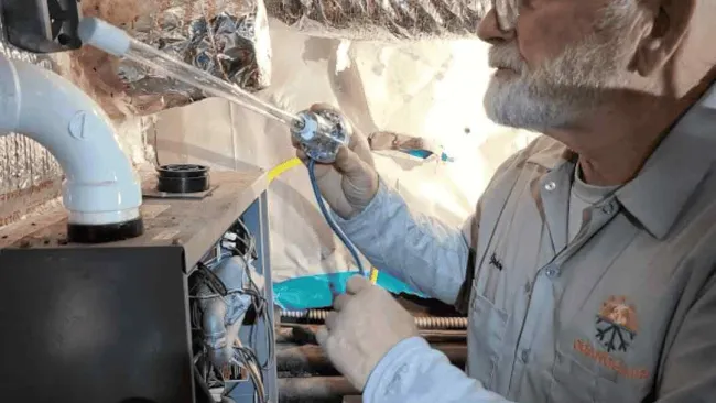 Technician inspecting and repairing HVAC system components in an insulated basement or crawlspace.