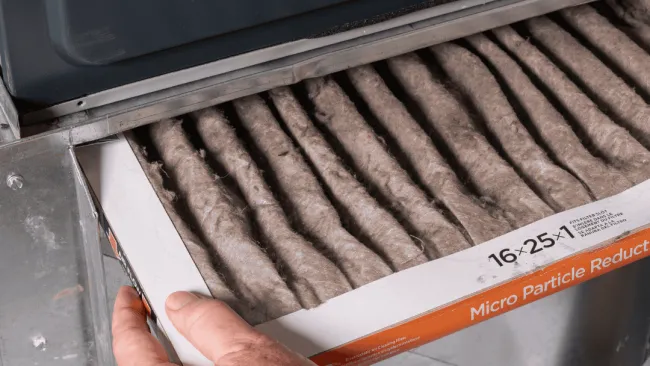 Person replacing a pleated air filter labeled 16x25x1 for micro particle reduction in HVAC system.