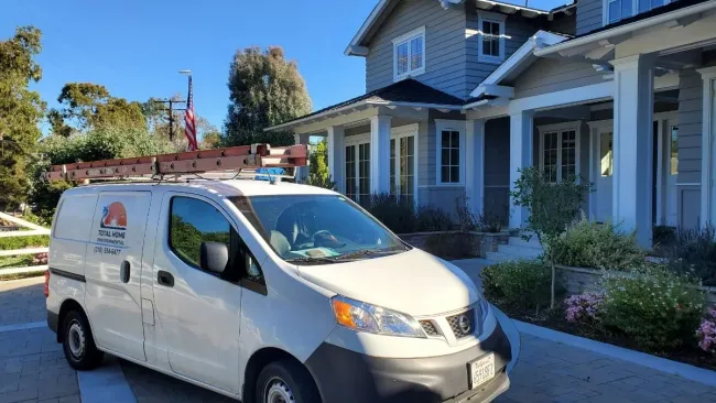 White service van with ladder on roof parked outside a modern house on a sunny day