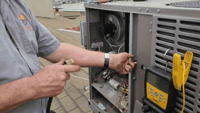 Technician servicing HVAC unit on rooftop using tools and diagnostic equipment on a partly cloudy day.