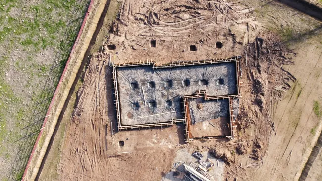 Aerial view of a building foundation construction site with wooden framework and concrete footings on cleared soil.