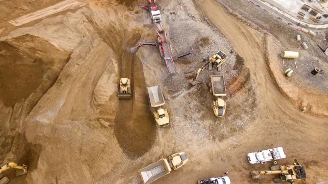 Aerial view of construction site with trucks, excavators, conveyor belt, and dirt piles during earthmoving work
