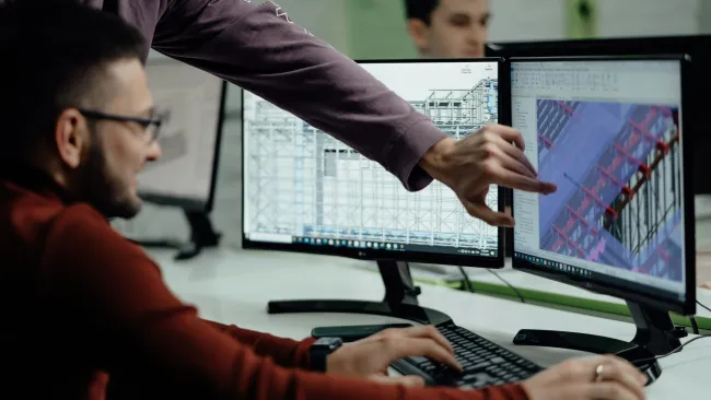Engineers collaborating on structural design displayed on dual monitors in an office setting.