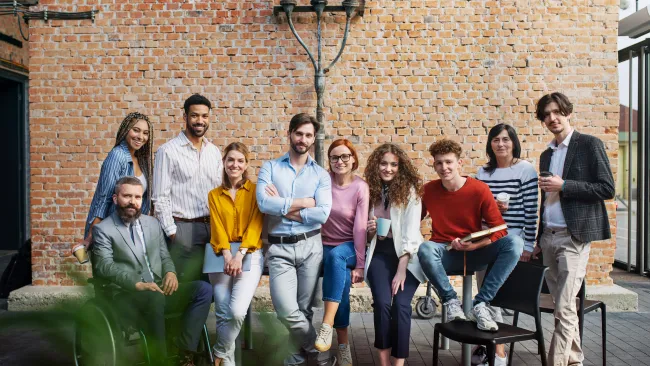 Diverse group of young professionals casually posing in front of a brick wall in a modern office patio