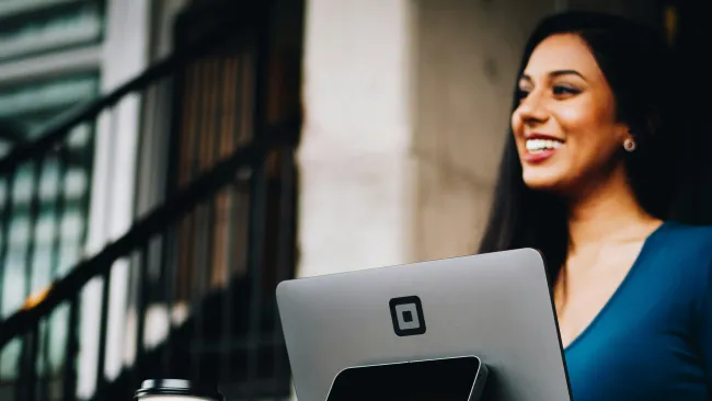 Smiling woman processing coffee purchase at a digital point-of-sale terminal in a cafe.