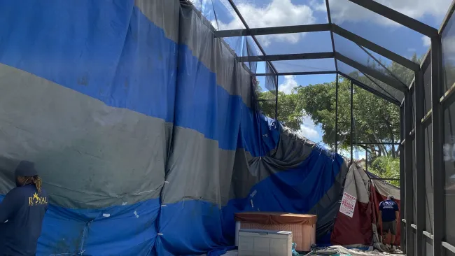 Indoor pool with blue water under a metal frame enclosure and large blue tarps covering one side during maintenance.