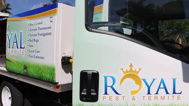 Royal Pest & Termite service truck with logo and list of pest control services parked outdoors under blue sky.