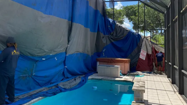 Pool area under a large tarp enclosure with workers preparing or repairing the screened patio.