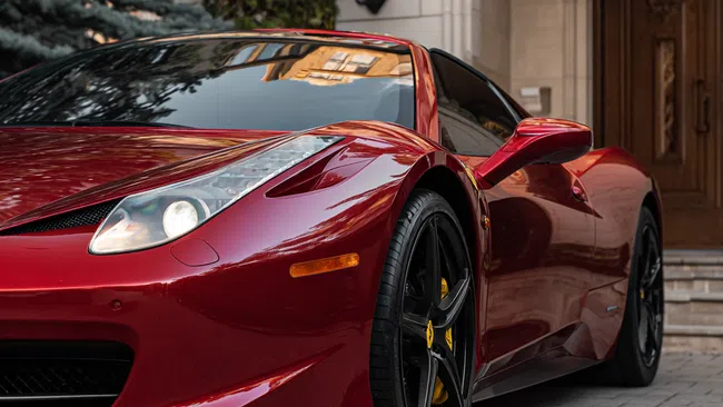 Red sports car with black rims parked in front of a luxurious building with wooden doors and stone pavement.