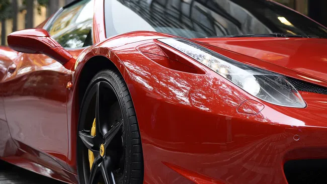 Close-up of a red luxury sports car front and side with black wheels parked on city street.