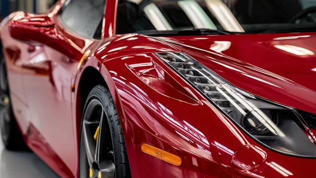 Close-up of a shiny red sports car front showing sleek headlights and detailed wheel in a showroom.