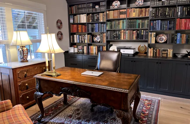 Classic home office with wooden desk, built-in bookshelves, decorative lamps and black leather chair