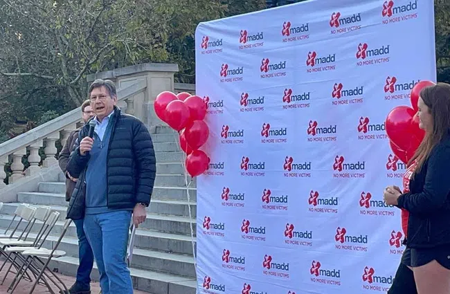 Man speaking at outdoor event with MADD banner and red balloons promoting no more victims campaign
