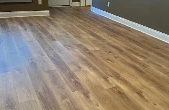 Empty room with natural wood flooring, brown walls, white trim, window with shutters, and a white door.