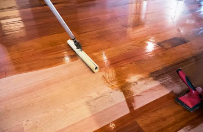 Applying wood stain on a hardwood floor with a roller showing the contrast between stained and unstained areas.