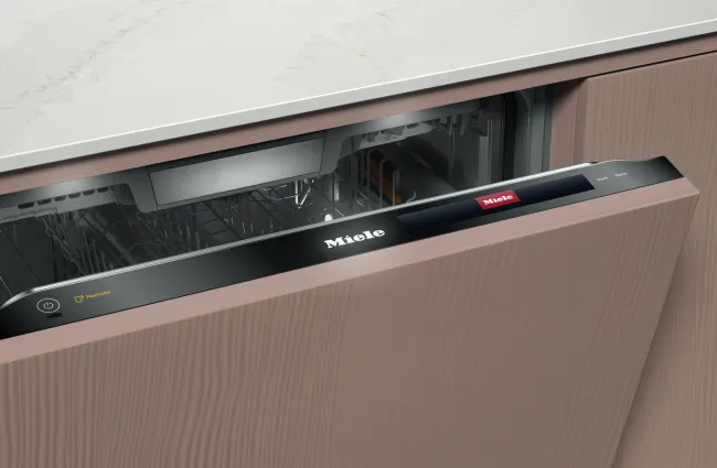 Open Miele dishwasher with modern wood paneling and digital control panel under marble countertop