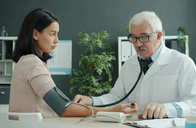 Doctor measuring blood pressure of a female patient in a medical office with medical equipment on the desk