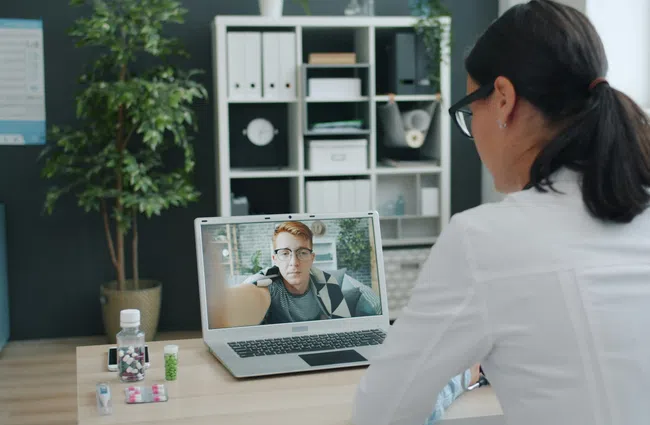 Medical professional conducts a video consultation with a patient using a laptop in a modern office setting.