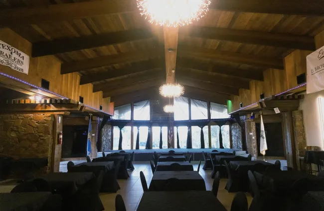 Spacious indoor event hall with wooden ceiling, black-covered tables, modern chandeliers, and large windows