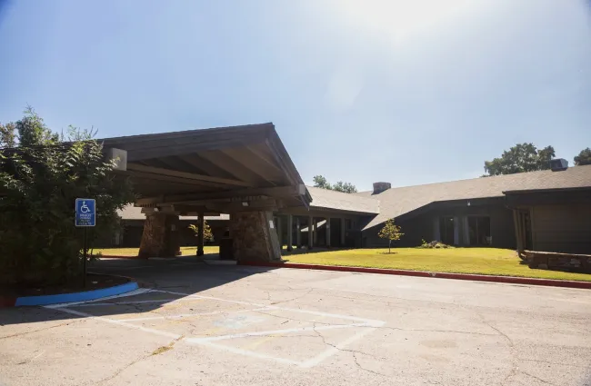 Modern building entrance with covered driveway, stone pillars, and handicap parking under bright clear sky.