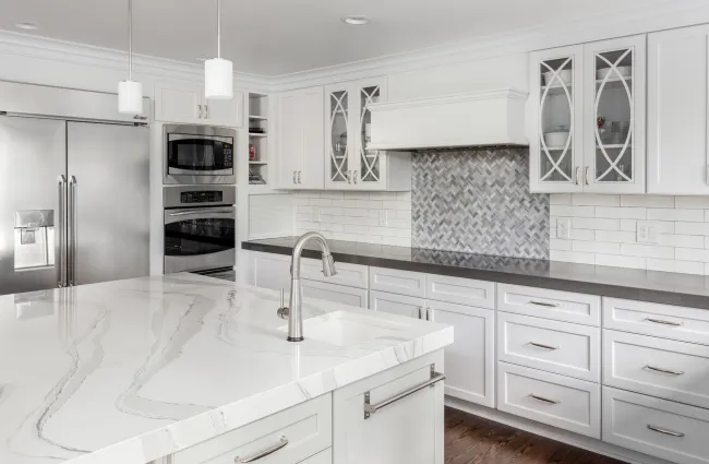 Modern white kitchen with marble island, stainless steel appliances, and grey backsplash tiles under white cabinets