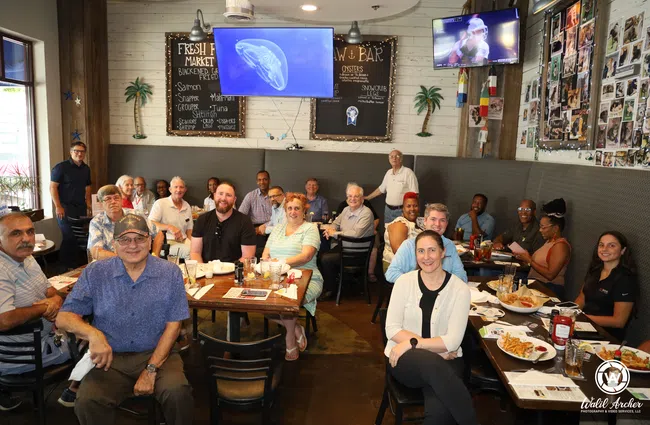 Group of diverse adults sitting and smiling in a casual restaurant with seafood menu and TV screens