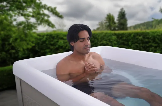 Man relaxing in an outdoor hot tub surrounded by greenery on a cloudy day.