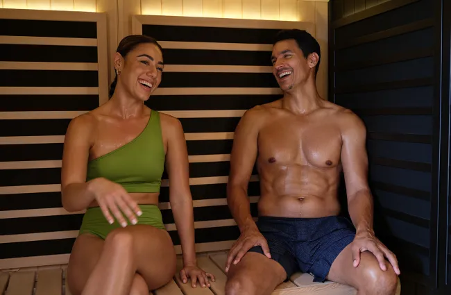 Smiling man and woman relaxing in sauna wearing swimwear, enjoying a healthy wellness moment together.