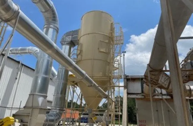 Industrial facility with large metal ducts and a central beige cylindrical storage silo under a clear blue sky