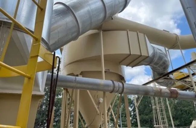 Industrial facility with large metal pipes and yellow ladder structure under a partly cloudy sky.