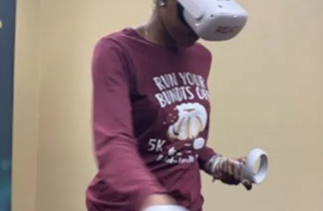 Person wearing virtual reality headset and holding VR controllers in an indoor setting with a blue bean bag.