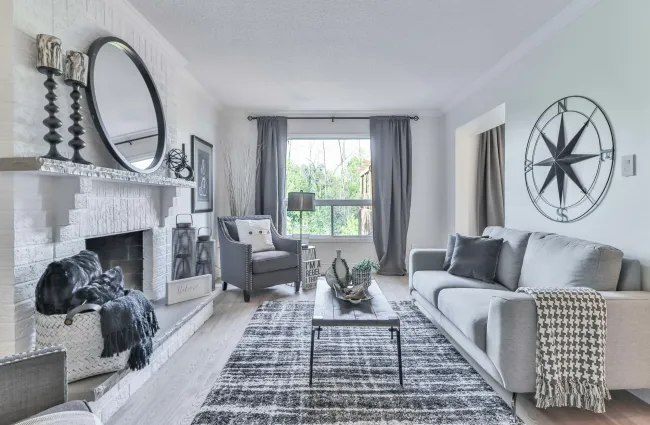 Modern gray and white living room with a fireplace, large window, armchair, sofa, and decorative wall art.
