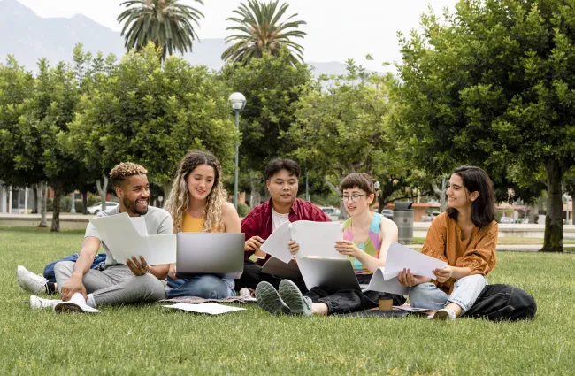 a group of people sitting on the grass with laptops